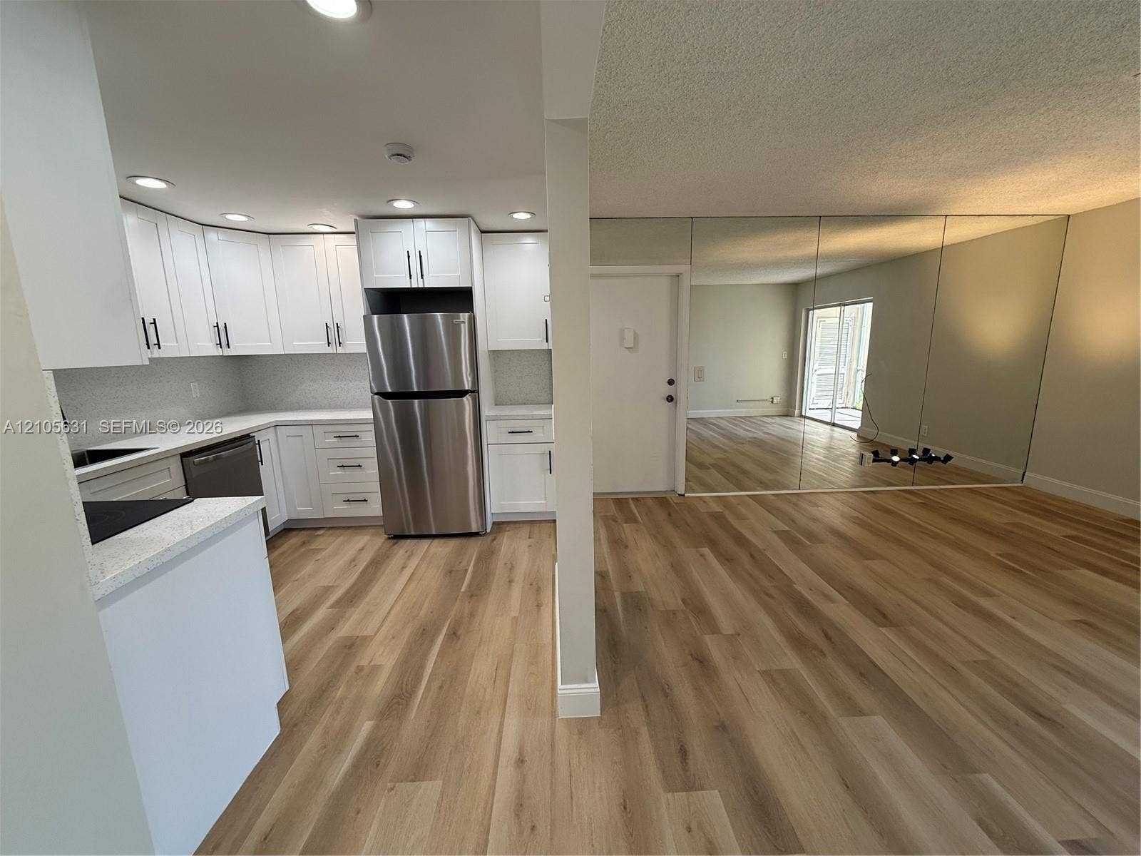 610 NW 13th Street, #0140, Boca Raton, FL 33486 Kitchen featuring white shaker-style cabinetry, stainless steel appliances, and solid-surface countertops, complemented by wood-finish flooring and full-height wall mirrors