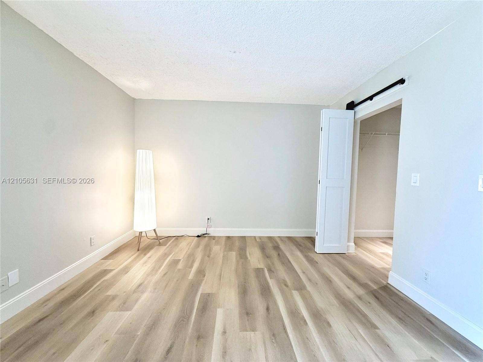 610 NW 13th Street, #0140, Boca Raton, FL 33486 Neutral interior space featuring wood-finish flooring, light-toned walls, and a white interior door on a black sliding track