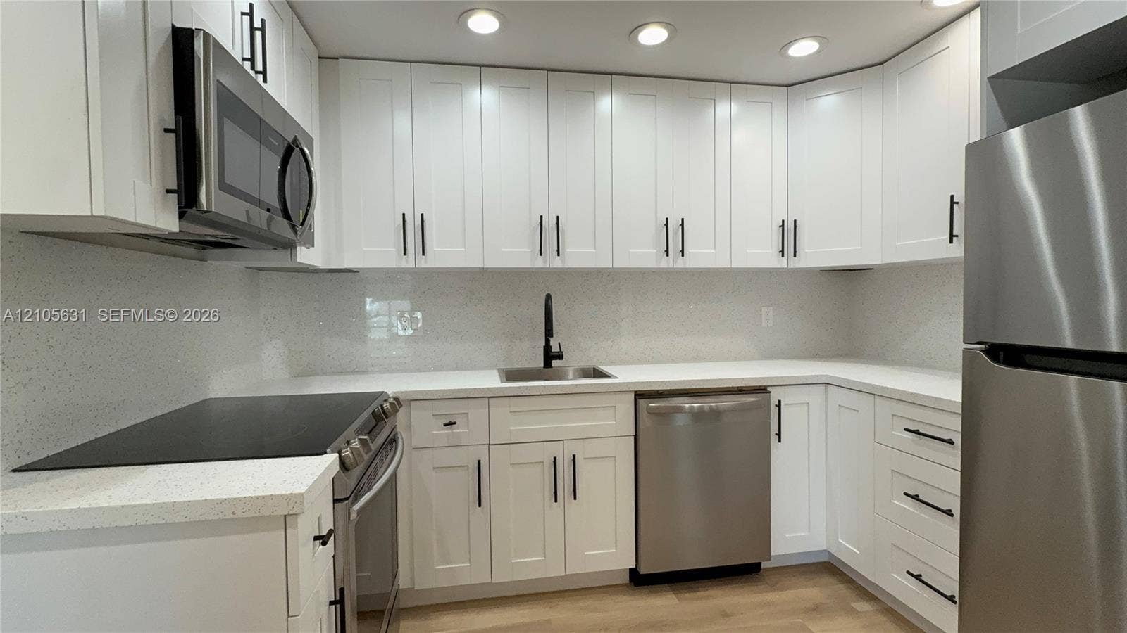 610 NW 13th Street, #0140, Boca Raton, FL 33486 Kitchen featuring white Shaker-style cabinetry, light-toned composite countertops, a full-height solid surface backsplash, stainless steel appliances, and matte black hardware