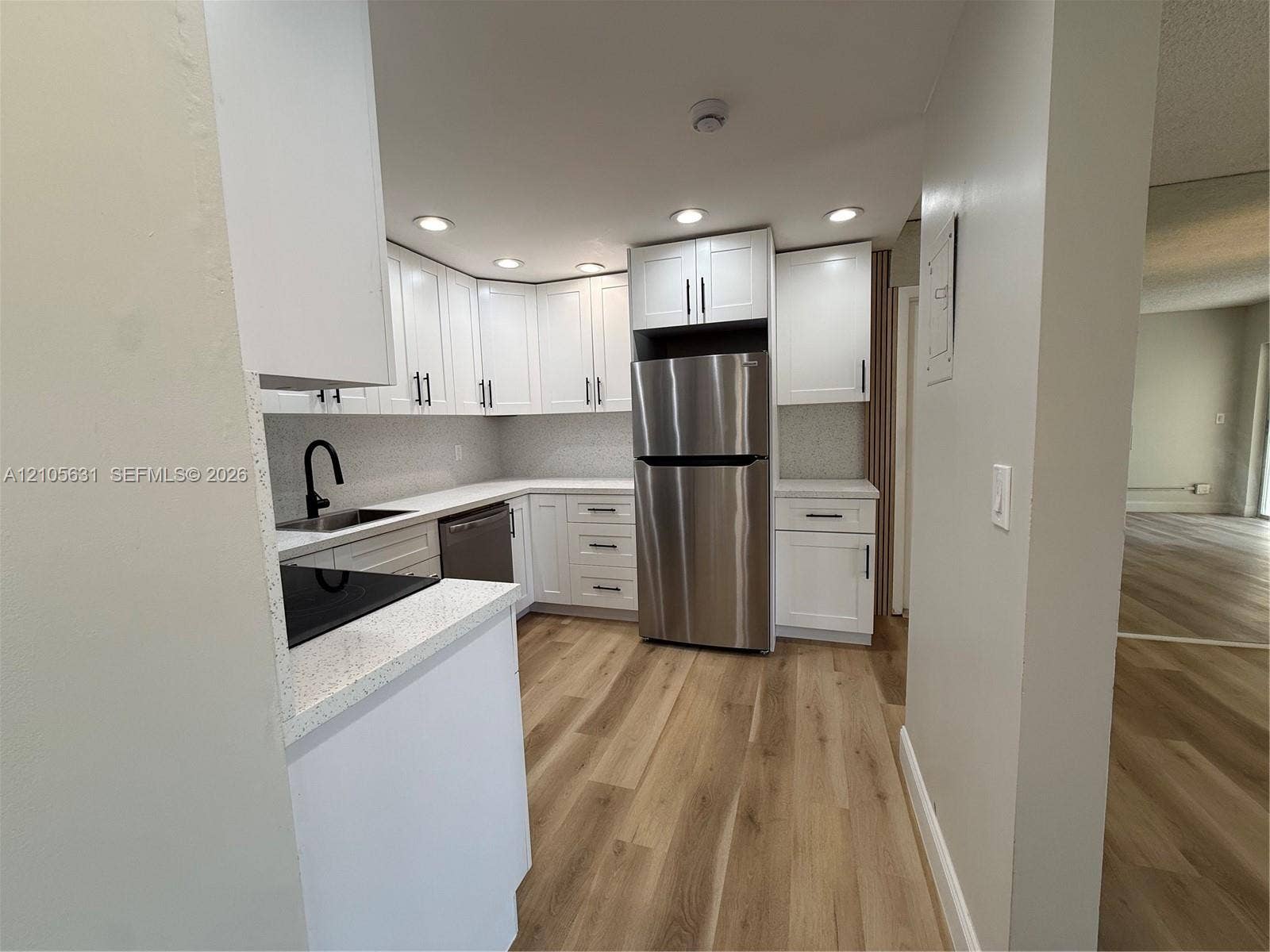 610 NW 13th Street, #0140, Boca Raton, FL 33486 Kitchen featuring white Shaker-style cabinetry, stainless steel appliances, light-toned stone-finish countertops, matte black plumbing fixtures, and wood-finish flooring