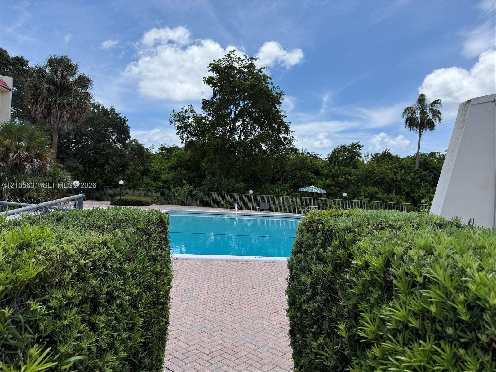 610 NW 13th Street, #0140, Boca Raton, FL 33486 Outdoor swimming pool featuring a brick paver deck, perimeter fencing, and mature shrubbery