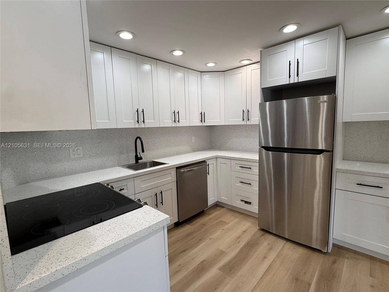 610 NW 13th Street, #0140, Boca Raton, FL 33486 Kitchen featuring white Shaker-style cabinetry, light-toned composite countertops, stainless steel appliances, matte black hardware, and wood-finish flooring