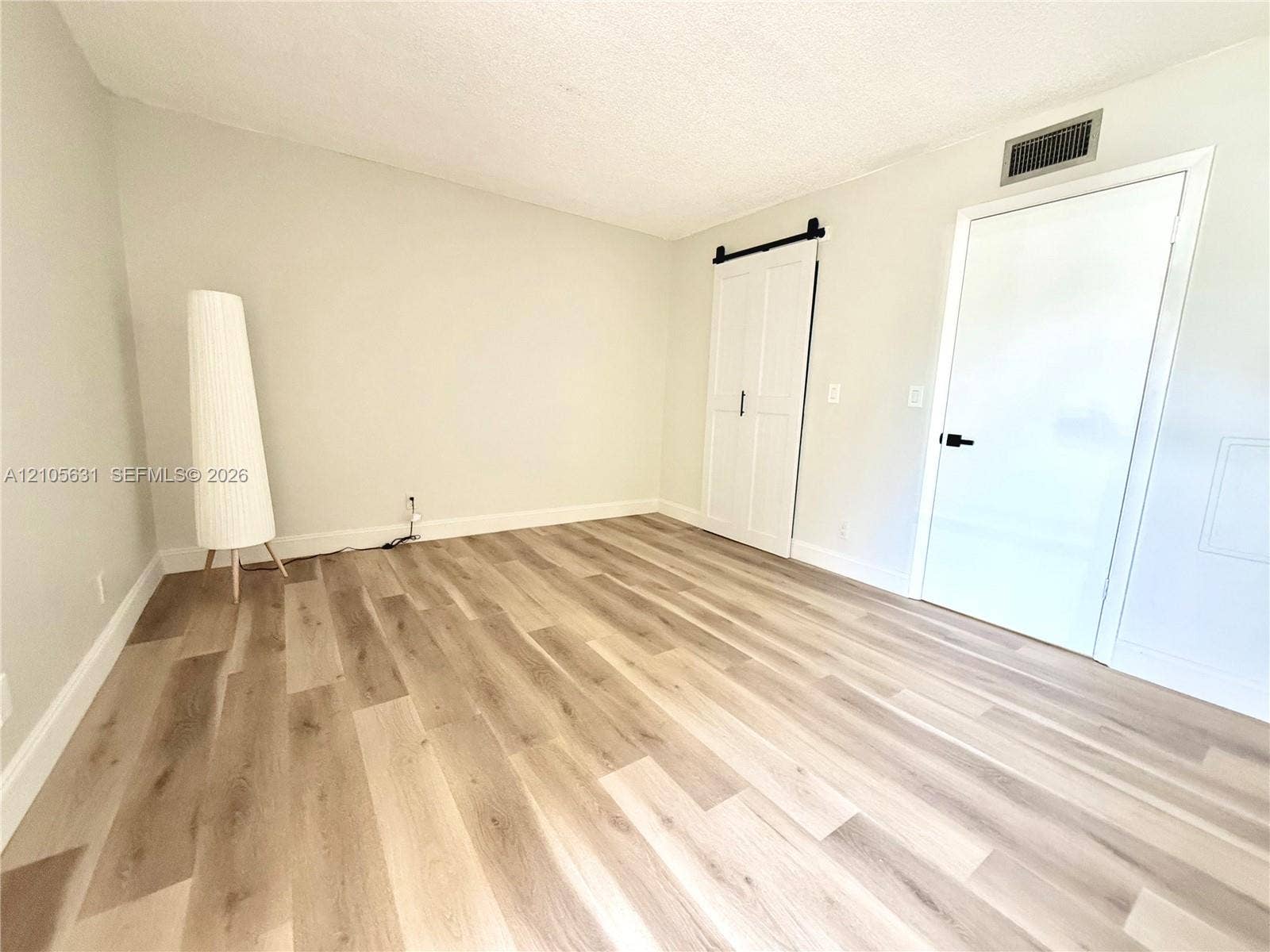 610 NW 13th Street, #0140, Boca Raton, FL 33486 Room featuring wood-finish flooring, white double sliding barn door with matte black hardware, and a solid-panel door with a matte black lever handle