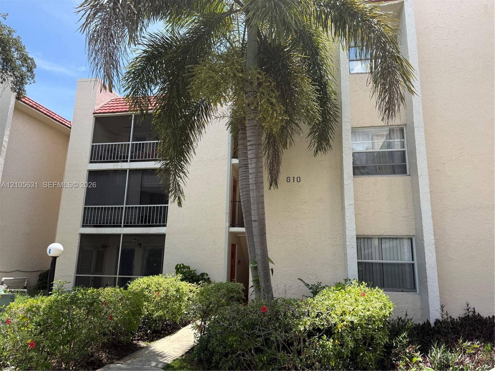 610 NW 13th Street, #0140, Boca Raton, FL 33486 Multi-story building exterior featuring a stucco facade, tiled roof, tiered screened-in balconies, and mature landscaping