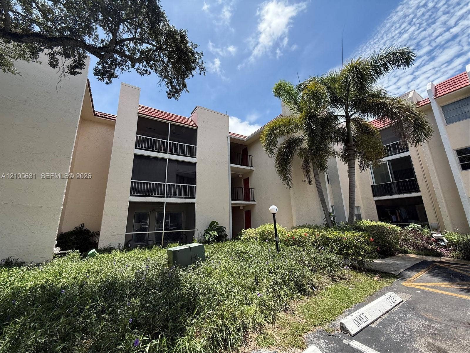 610 NW 13th Street, #0140, Boca Raton, FL 33486 Multi-story stucco exterior featuring screened balconies, red tile roofing, and mature palm tree landscaping