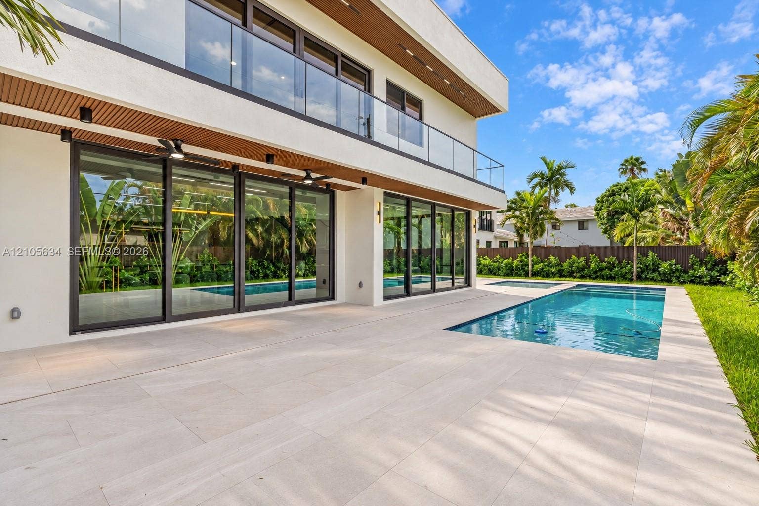 623 NE 16th Terrace, Fort Lauderdale, FL 33304 Modern exterior featuring a wrap-around glass balcony, oversized floor-to-ceiling sliding glass doors, a stone-tiled patio, and an in-ground swimming pool
