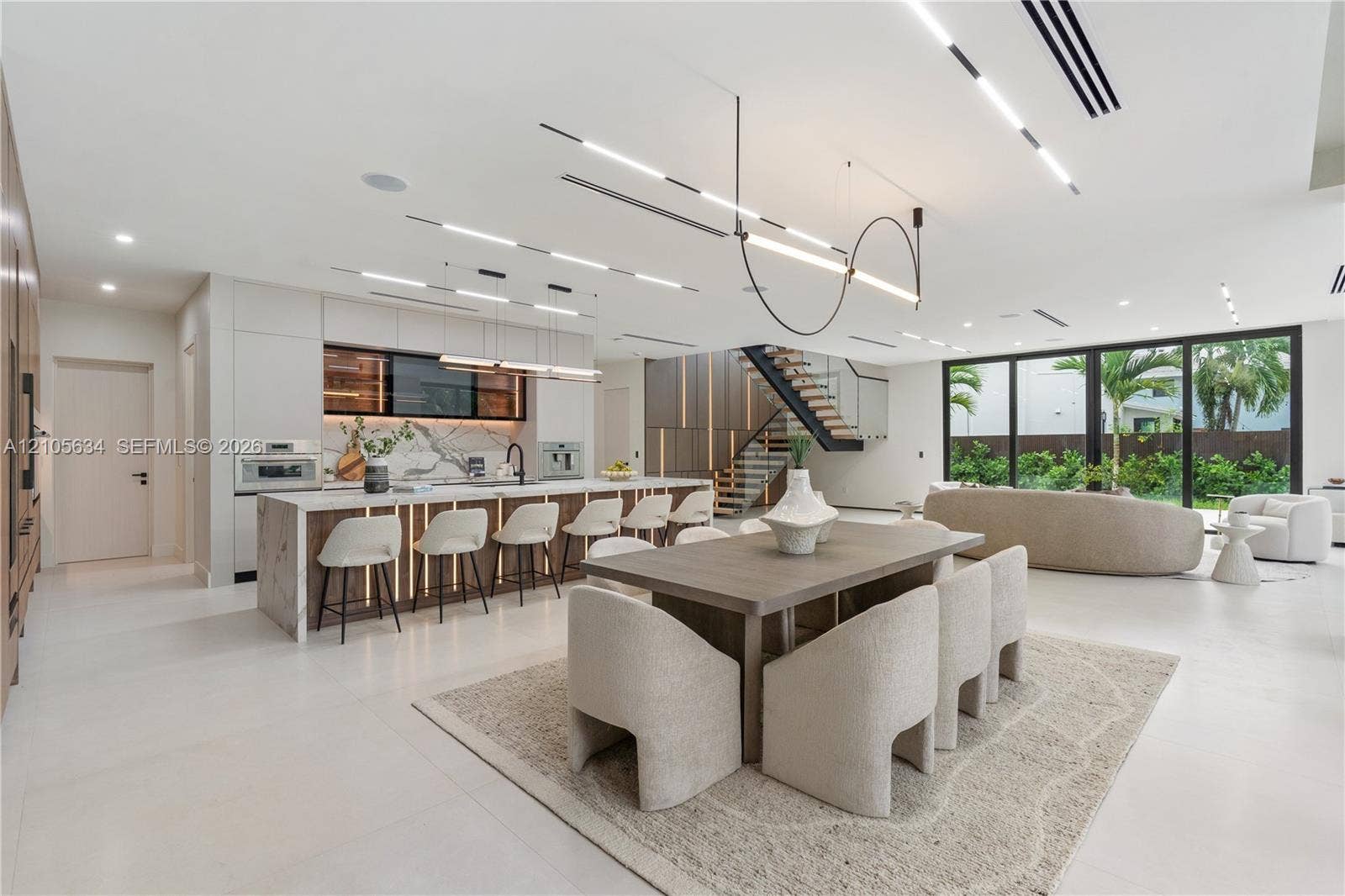 623 NE 16th Terrace, Fort Lauderdale, FL 33304 Open-concept interior featuring large-format flooring, a kitchen island with stone-surface counters, integrated LED accent lighting, floating staircase with metal railings, and floor-to-ceiling glass panel walls