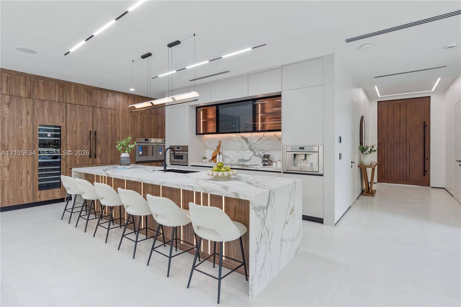 623 NE 16th Terrace, Fort Lauderdale, FL 33304 Modern kitchen featuring flat-panel wood-finish cabinetry, a large waterfall island with stone countertop, built-in stainless steel appliances, integrated under-cabinet lighting, and recessed linear ceiling illumination