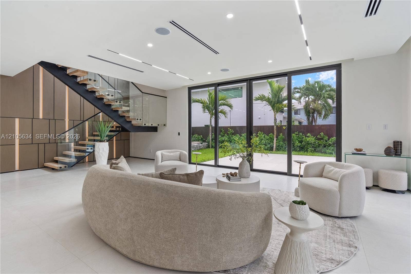 623 NE 16th Terrace, Fort Lauderdale, FL 33304 Open-concept interior featuring large-format tile flooring, a custom metal staircase with a glass railing, built-in decorative wall paneling, and floor-to-ceiling sliding glass doors