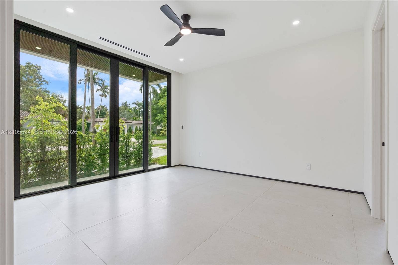 623 NE 16th Terrace, Fort Lauderdale, FL 33304 Large-format tile flooring, multi-panel sliding glass doors with dark frames, matte black ceiling fan, and recessed lighting
