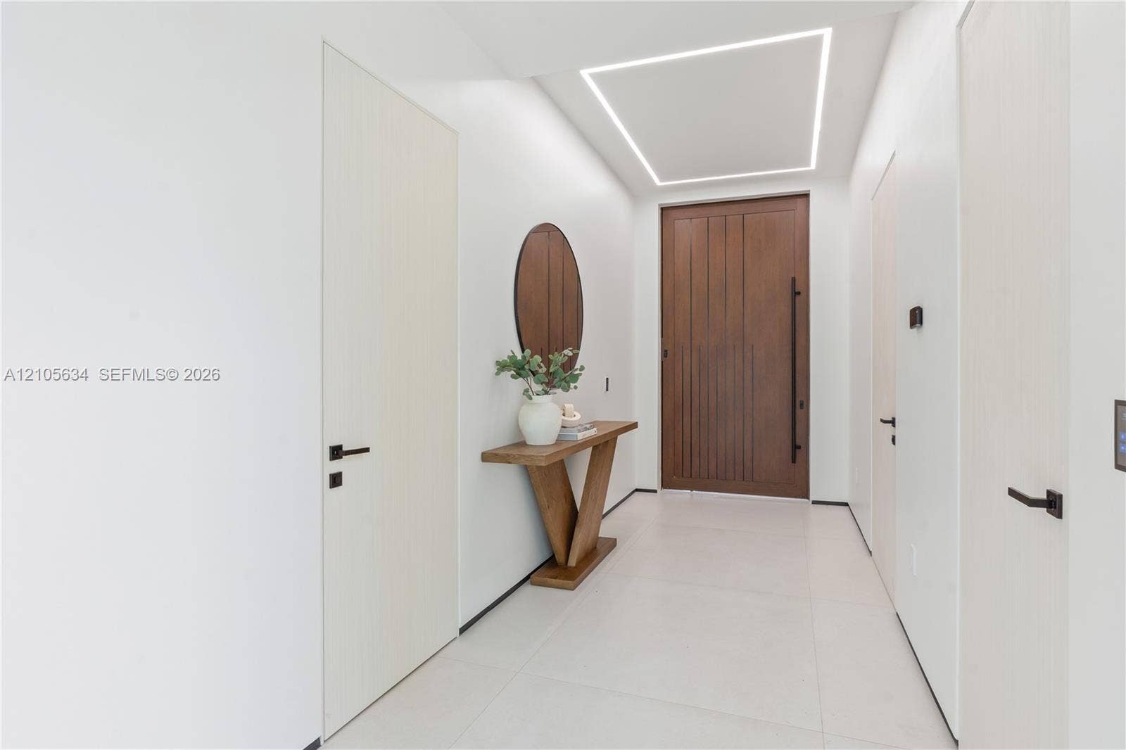 623 NE 16th Terrace, Fort Lauderdale, FL 33304 Entryway featuring a large-format wood-finish front door with a vertical pull handle, recessed linear ceiling lighting, minimalist flat-panel interior doors with matte black hardware, and large-format porcelain tile flooring