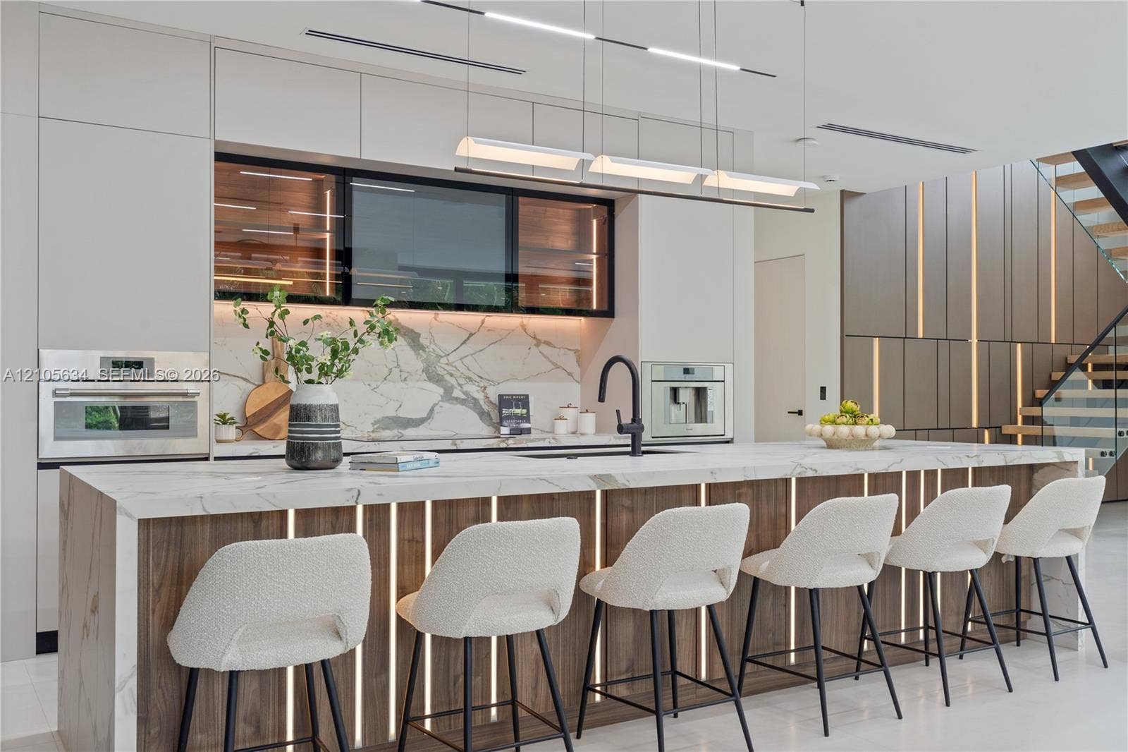 623 NE 16th Terrace, Fort Lauderdale, FL 33304 Contemporary kitchen featuring a stone-surface waterfall island with integrated vertical lighting, flat-panel cabinetry, a stone backsplash, built-in stainless steel appliances, and linear pendant lighting