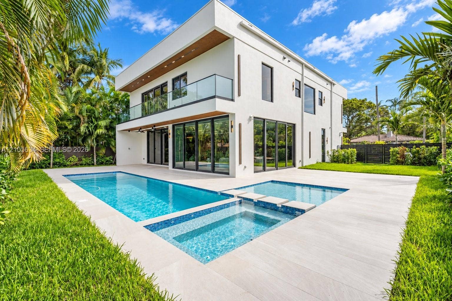 623 NE 16th Terrace, Fort Lauderdale, FL 33304 Modern two-story architectural exterior featuring smooth stucco finishes, floor-to-ceiling glass panel doors, a second-level glass-railed balcony, and an integrated swimming pool and spa surrounded by light-toned hardscaping
