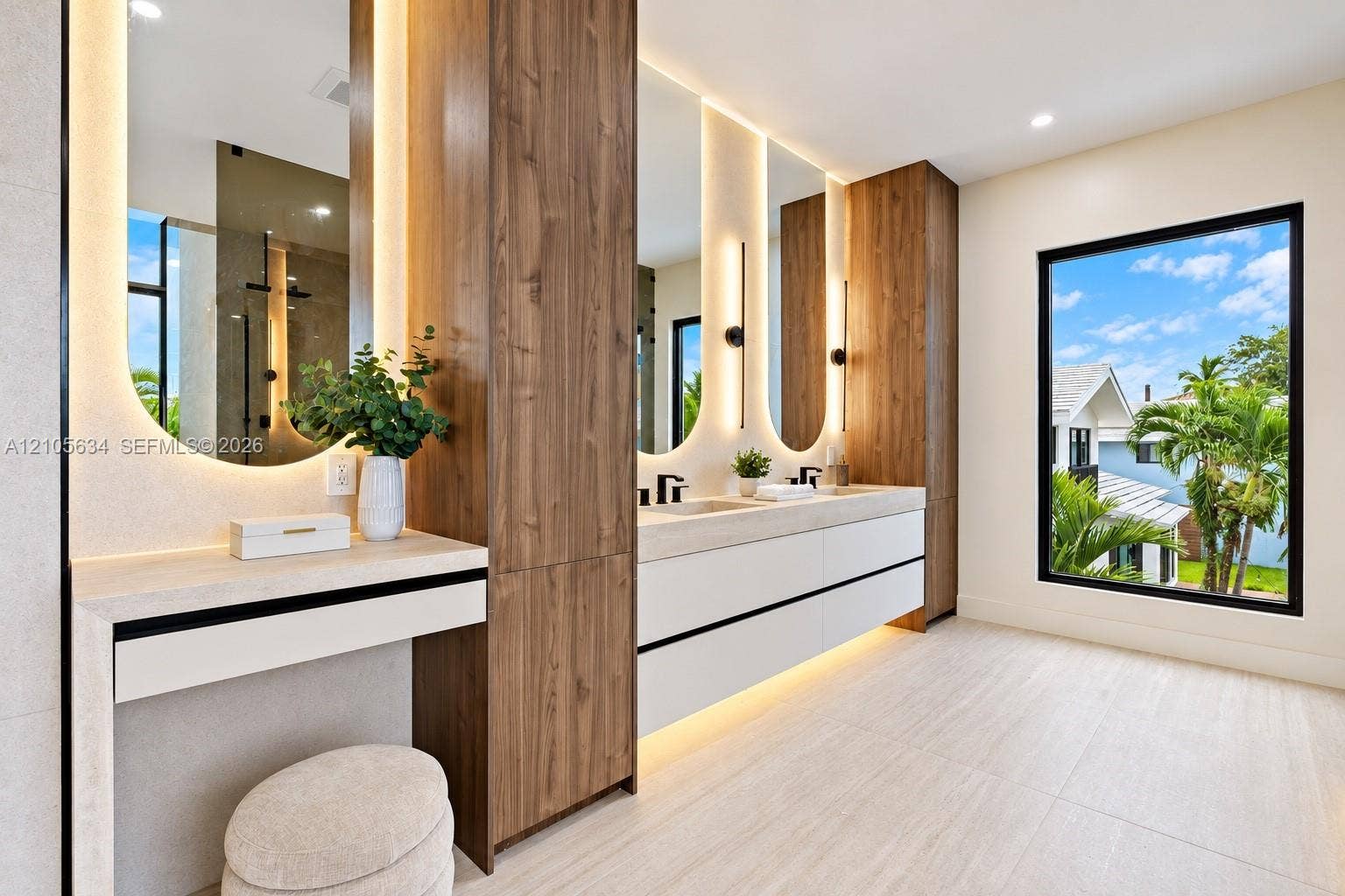 623 NE 16th Terrace, Fort Lauderdale, FL 33304 Floating double vanity with integrated wood-finish cabinetry, arched mirrors with perimeter lighting, stone-top surfaces, and matte black fixtures