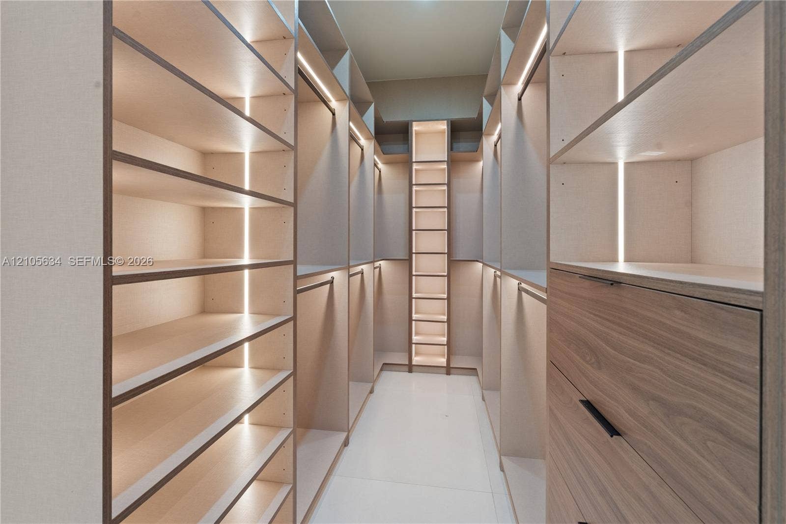 623 NE 16th Terrace, Fort Lauderdale, FL 33304 Walk-in wardrobe featuring custom cabinetry with wood-finish drawer fronts, open shelving, integrated vertical LED lighting, and matte black hardware