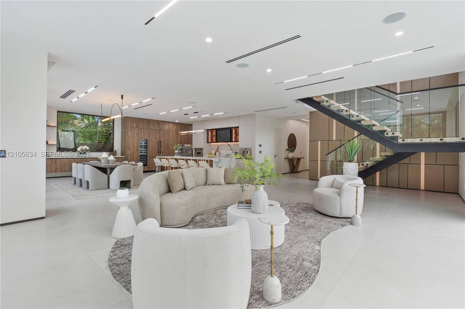 623 NE 16th Terrace, Fort Lauderdale, FL 33304 Open-concept floor plan featuring expansive stone-tile flooring, recessed linear lighting, custom wood-paneled cabinetry, and a floating staircase with glass railings