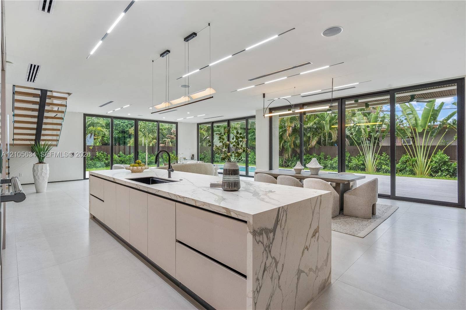 623 NE 16th Terrace, Fort Lauderdale, FL 33304 Kitchen featuring a large central island with waterfall-edge stone countertops, custom flat-panel cabinetry, matte black hardware, floor-to-ceiling multi-panel sliding glass doors, and recessed linear LED ceiling lighting