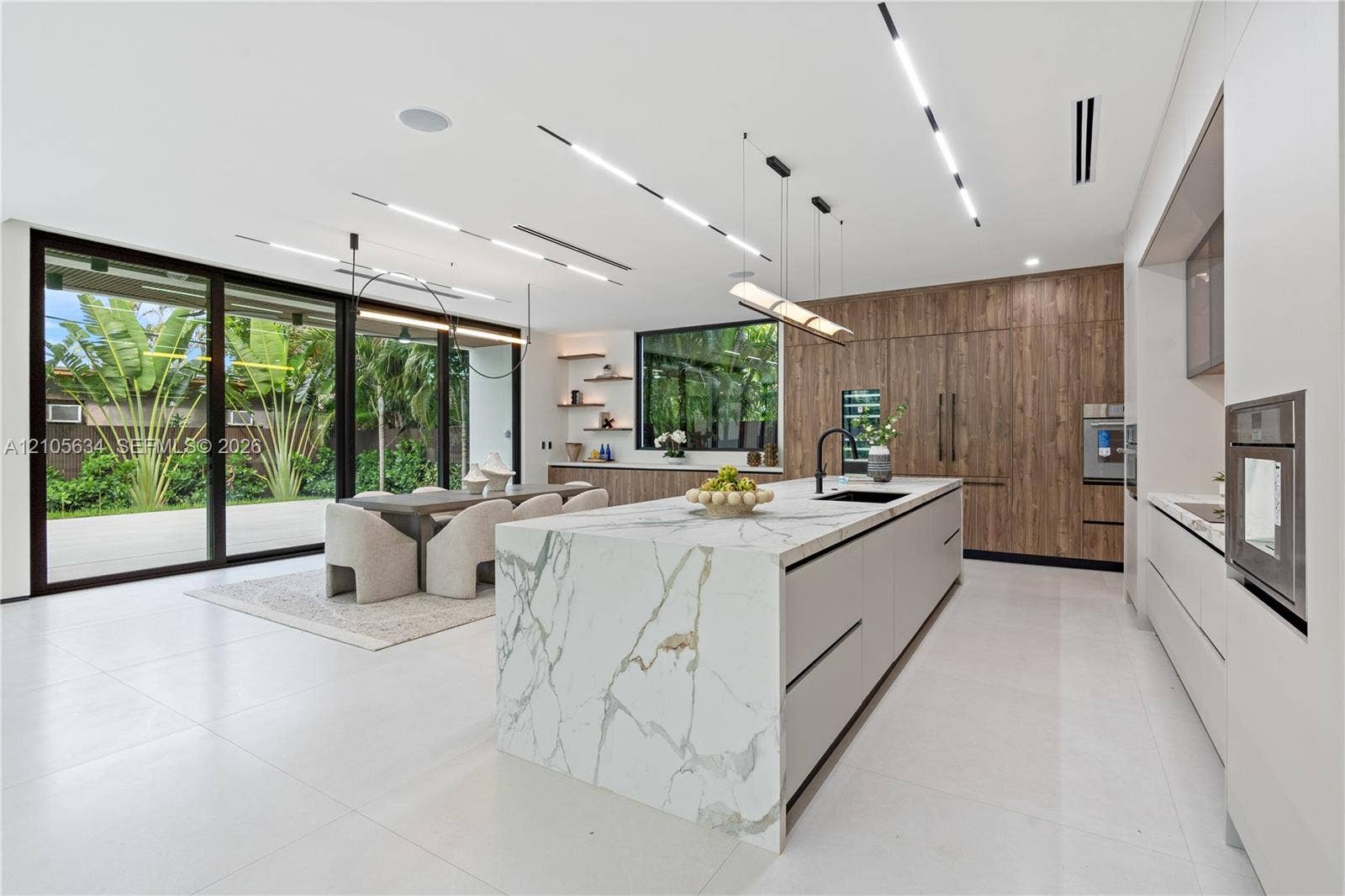 623 NE 16th Terrace, Fort Lauderdale, FL 33304 Kitchen featuring an oversized island with stone-finish waterfall countertop, wood-finish cabinetry, floor-to-ceiling glass sliding doors, integrated linear lighting, and large-format tile flooring