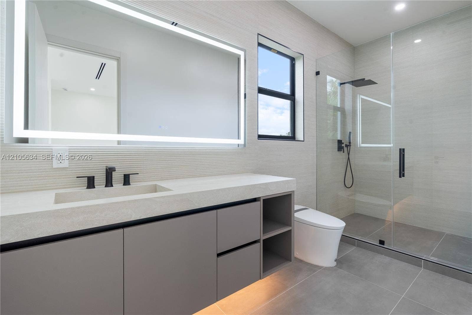 623 NE 16th Terrace, Fort Lauderdale, FL 33304 Floating vanity with integrated sink, stone-finish countertop, under-cabinet lighting, LED-backlit mirror, and glass-enclosed walk-in shower with matte black rainfall fixture