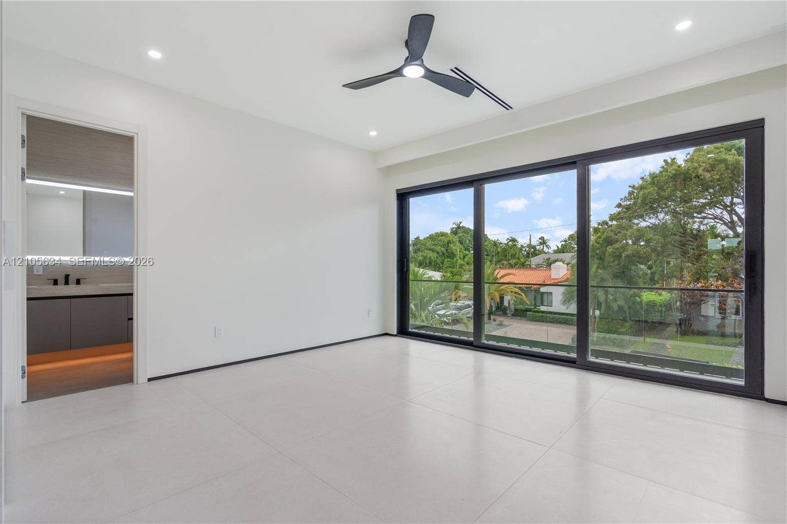 623 NE 16th Terrace, Fort Lauderdale, FL 33304 Large-format porcelain tile flooring, expansive floor-to-ceiling sliding glass doors with black frames, recessed LED lighting, three-blade ceiling fan, and balcony with glass railing
