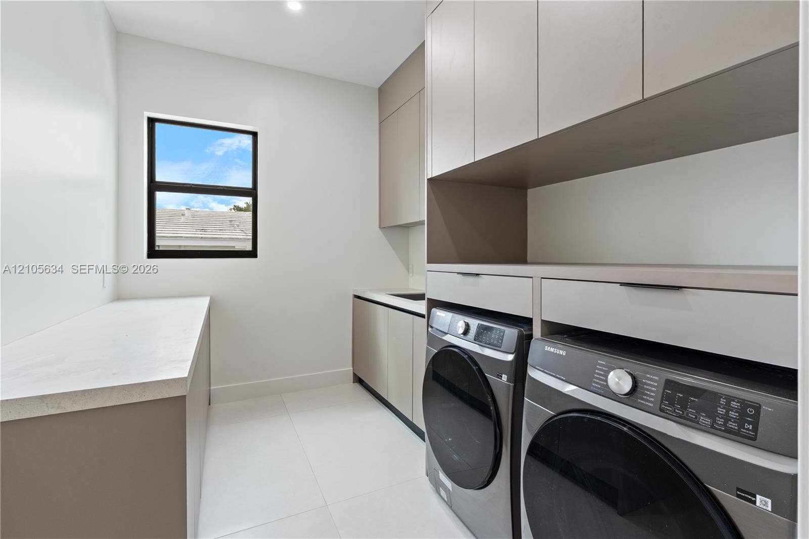 623 NE 16th Terrace, Fort Lauderdale, FL 33304 Laundry area featuring custom flat-panel cabinetry, light-toned stone-finish countertops, tile flooring, and integrated laundry appliances