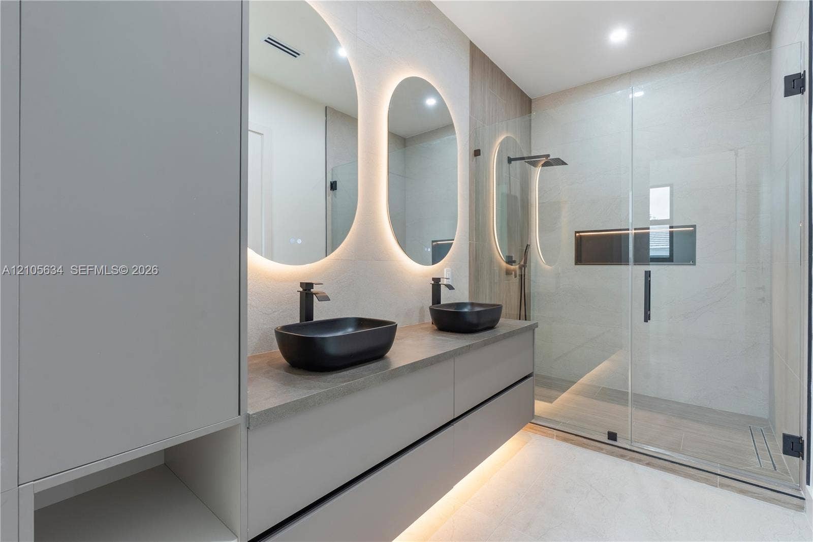 623 NE 16th Terrace, Fort Lauderdale, FL 33304 Floating dual-sink vanity with matte black fixtures, quartz-finish countertop, backlit oval mirrors, and a walk-in glass-enclosed shower featuring a built-in recessed niche