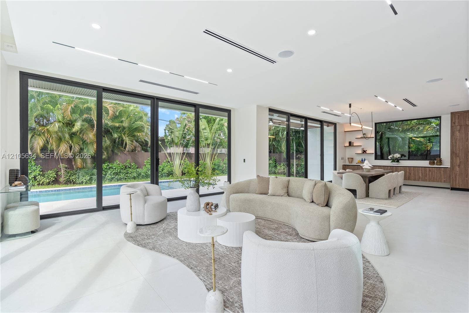 623 NE 16th Terrace, Fort Lauderdale, FL 33304 Open-concept interior featuring large-format flooring, expansive floor-to-ceiling sliding glass doors, recessed linear lighting, and built-in wood cabinetry