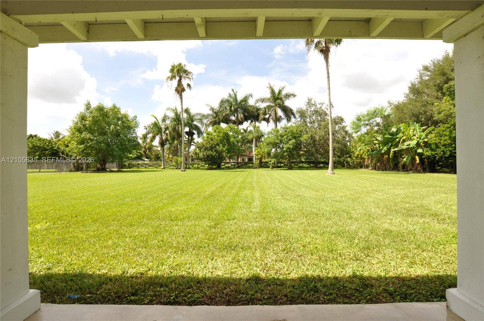 16760 SW 280th Street, Homestead, FL 33031 Expansive backyard featuring a large grass lawn, mature palm trees, perimeter fencing, and a covered porch with structural columns
