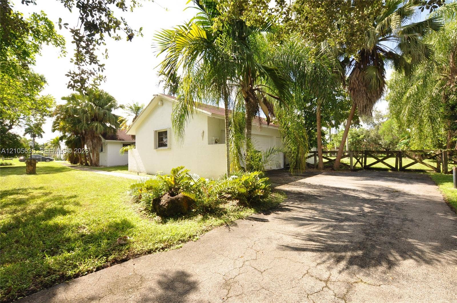 16760 SW 280th Street, Homestead, FL 33031 Stucco exterior, multi-car garage, asphalt driveway, timber cross-buck fencing, and established tropical landscaping