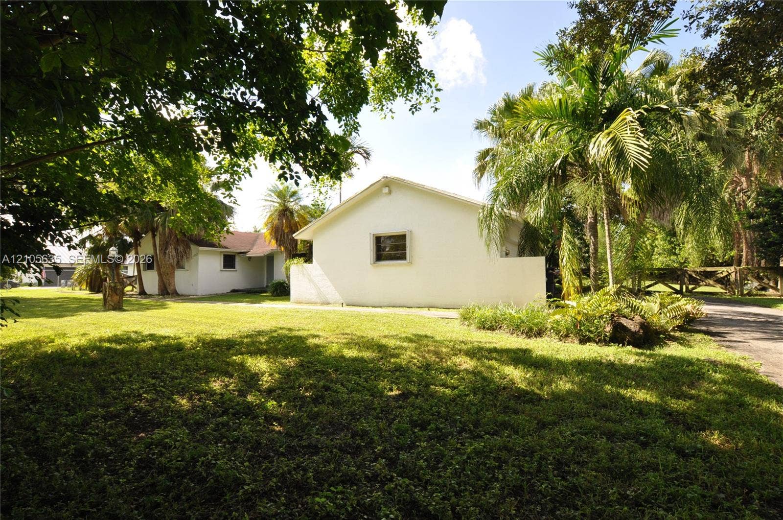 16760 SW 280th Street, Homestead, FL 33031 Stucco exterior residence featuring a sprawling lawn, mature palm trees, perimeter wooden fencing, and a paved driveway