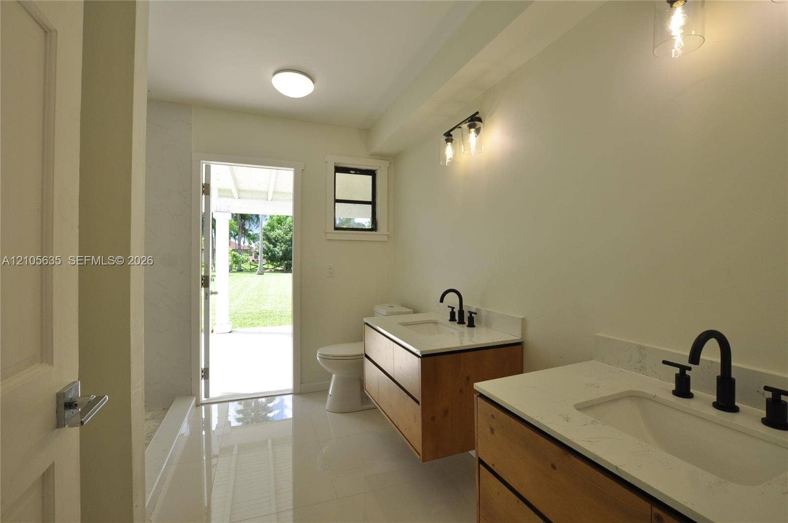 16760 SW 280th Street, Homestead, FL 33031 Dual floating vanities featuring light-tone wood-finish cabinetry, white stone-composite countertops, rectangular under-mount sinks, and matte black widespread faucets