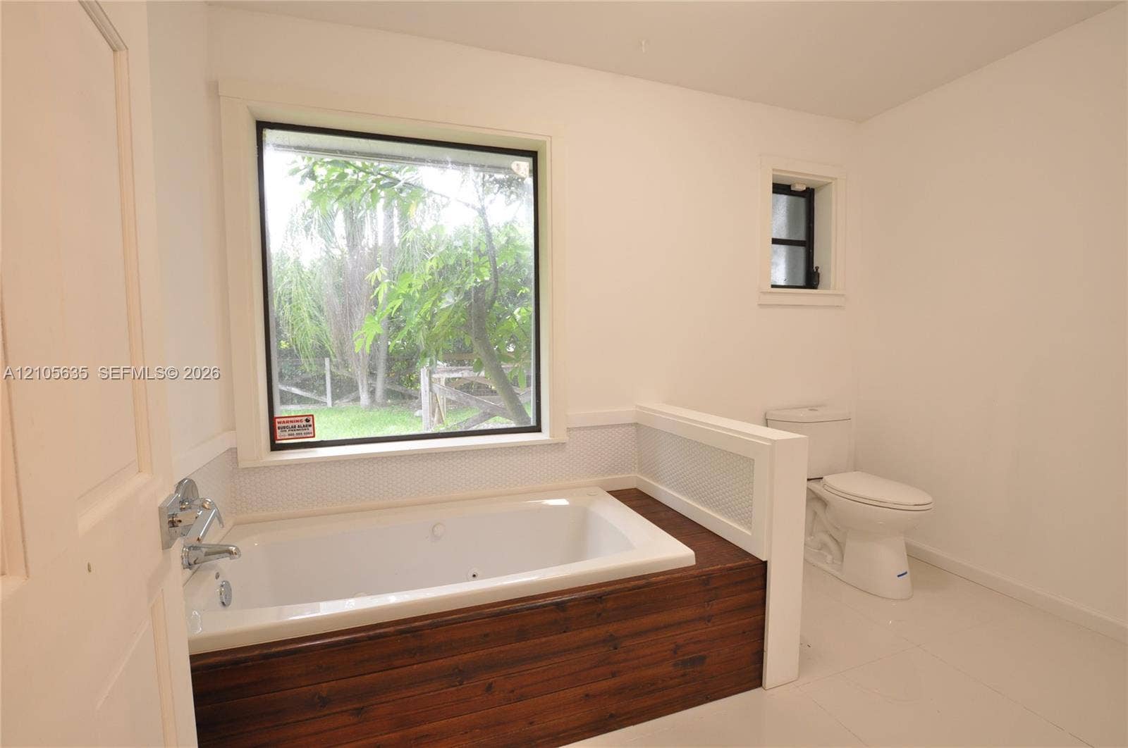 16760 SW 280th Street, Homestead, FL 33031 Built-in soaking tub with wood-finish surround, large window with exterior landscape, tile flooring, and crisp white wall finish