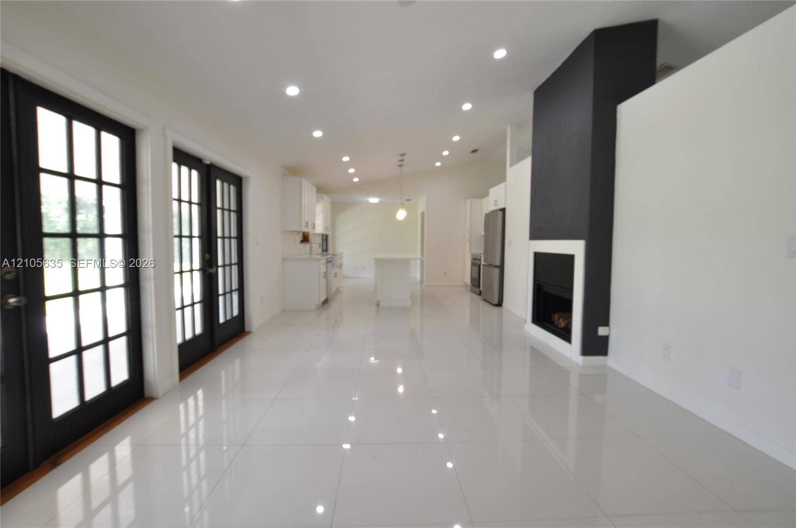 16760 SW 280th Street, Homestead, FL 33031 Open interior featuring white tile flooring, recessed lighting, double French doors with black frames, and a floor-to-ceiling fireplace with a contrast hearth