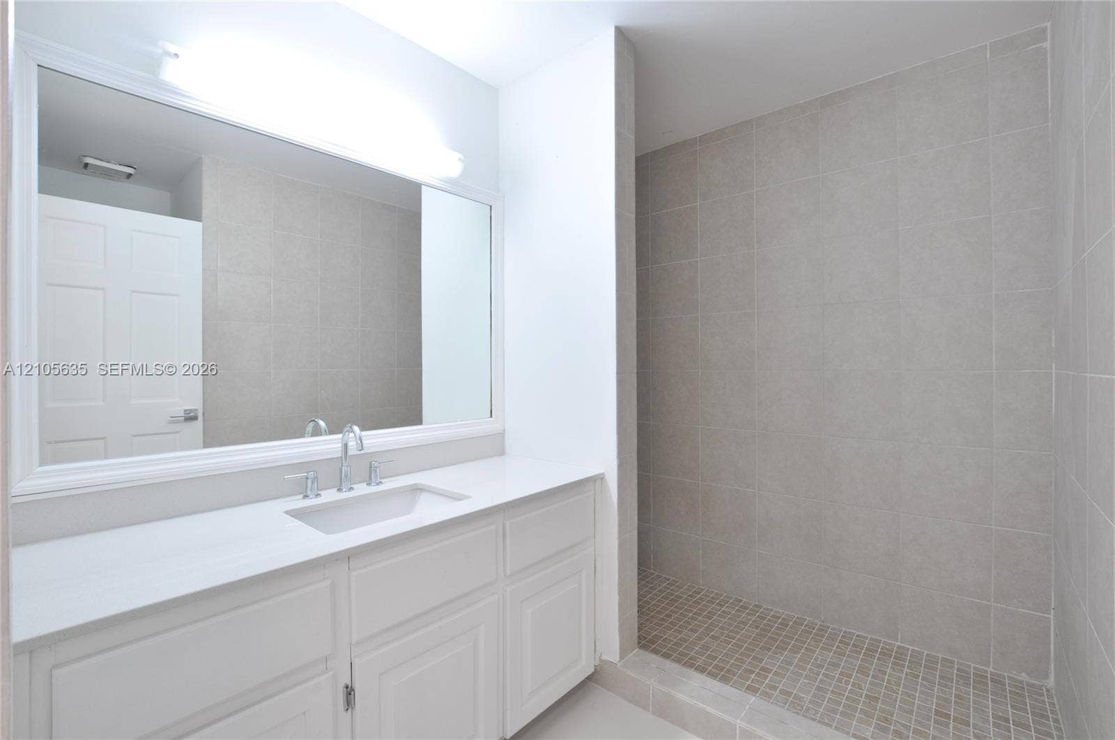 16760 SW 280th Street, Homestead, FL 33031 Bathroom featuring a white vanity cabinet with a solid surface countertop, undermount sink, expansive wall-mounted mirror, and a walk-in shower with floor-to-ceiling tile surround