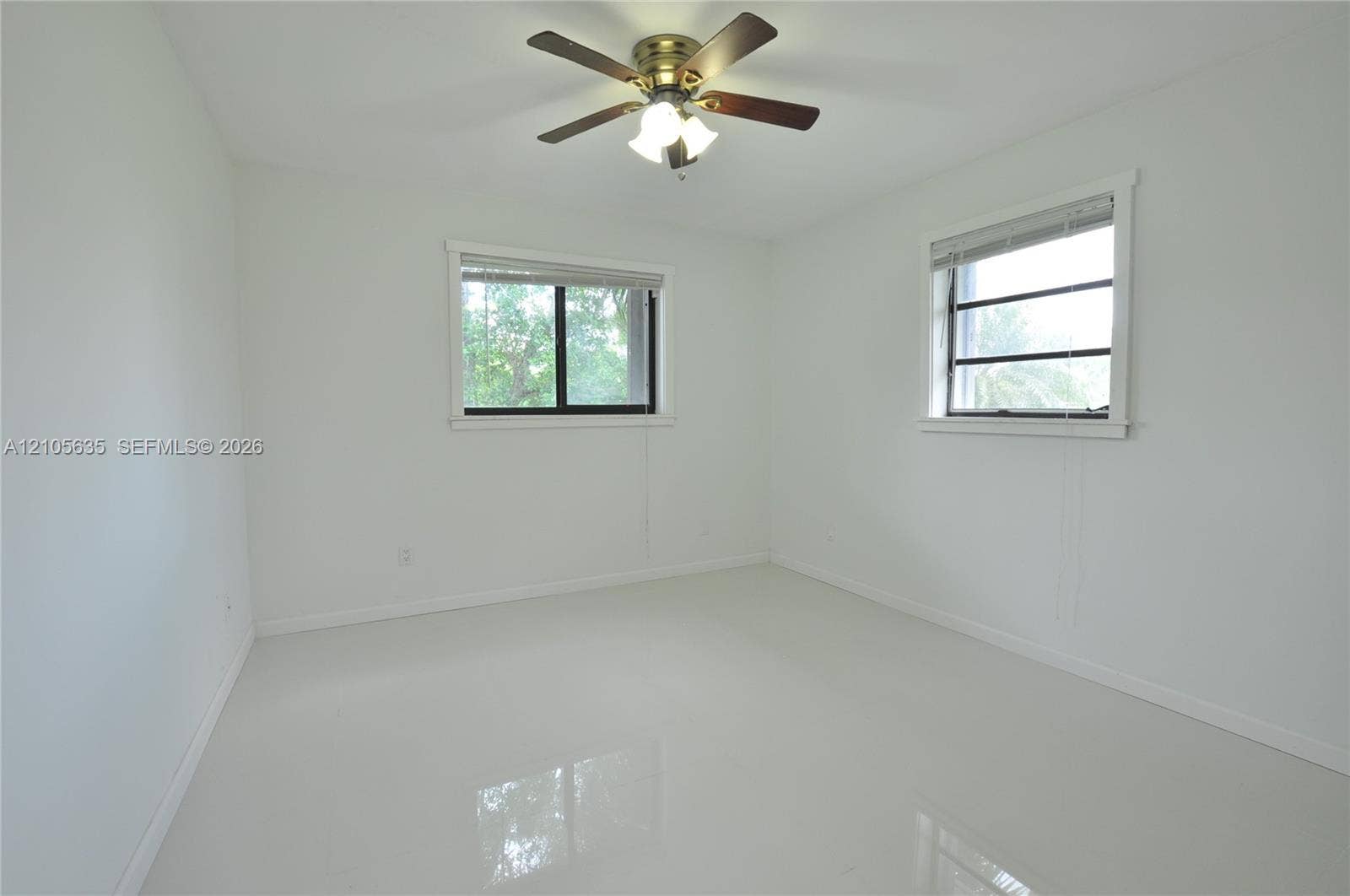 16760 SW 280th Street, Homestead, FL 33031 Neutral-toned interior space featuring light-colored tile flooring, two windows with horizontal blinds, and a multi-blade ceiling fan with integrated lighting