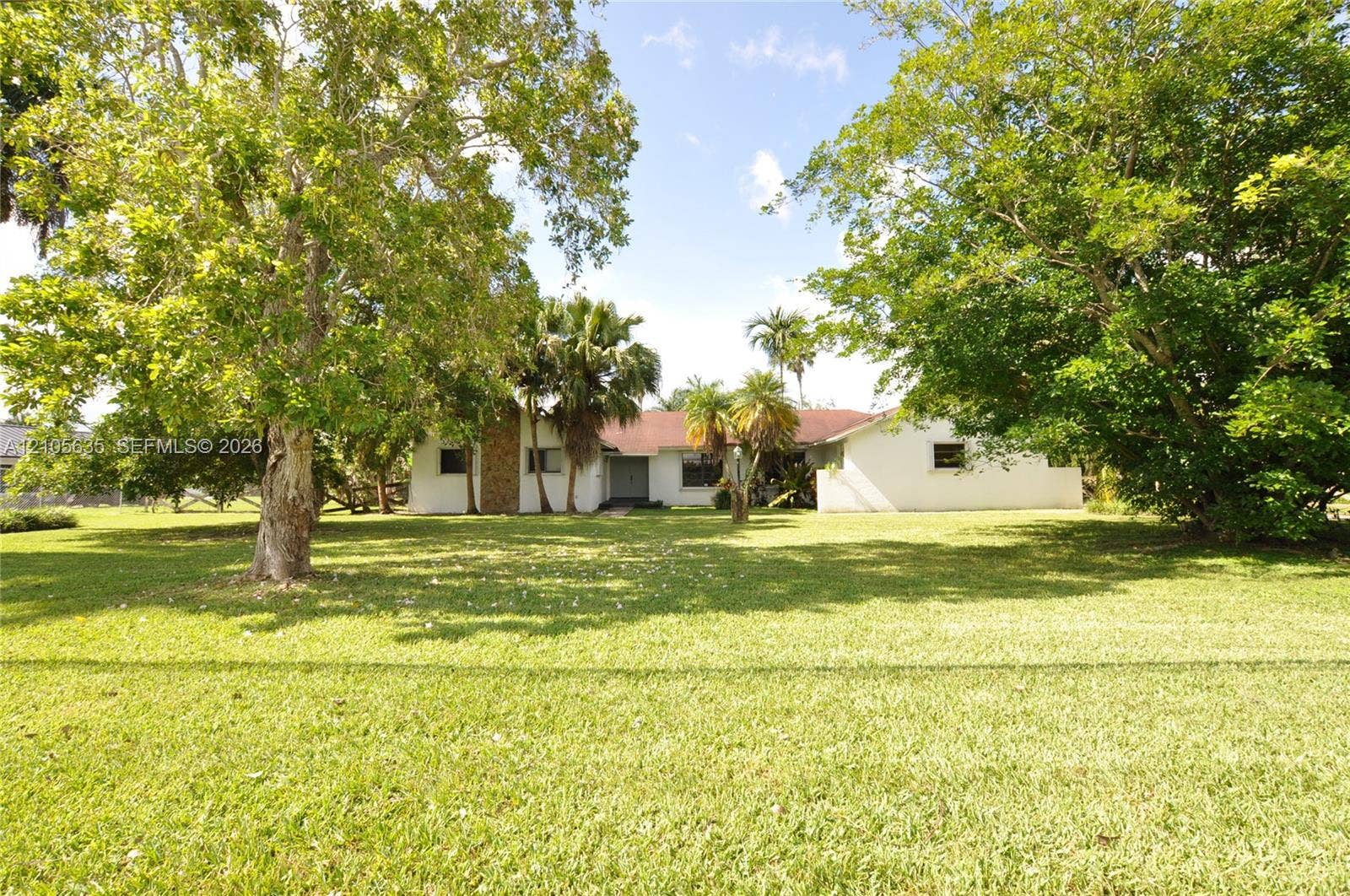 16760 SW 280th Street, Homestead, FL 33031 Expansive lawn with mature trees and palms, featuring a white exterior residence with stone-clad masonry detail and a shingled roof