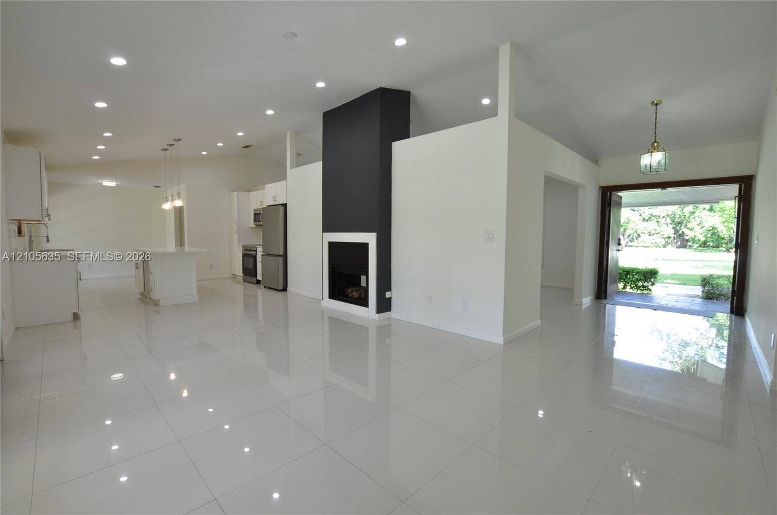 16760 SW 280th Street, Homestead, FL 33031 Open-concept interior featuring large-format polished tile flooring, vaulted ceilings with recessed lighting, a modern floor-to-ceiling fireplace with high-contrast surround, and stainless steel kitchen appliances