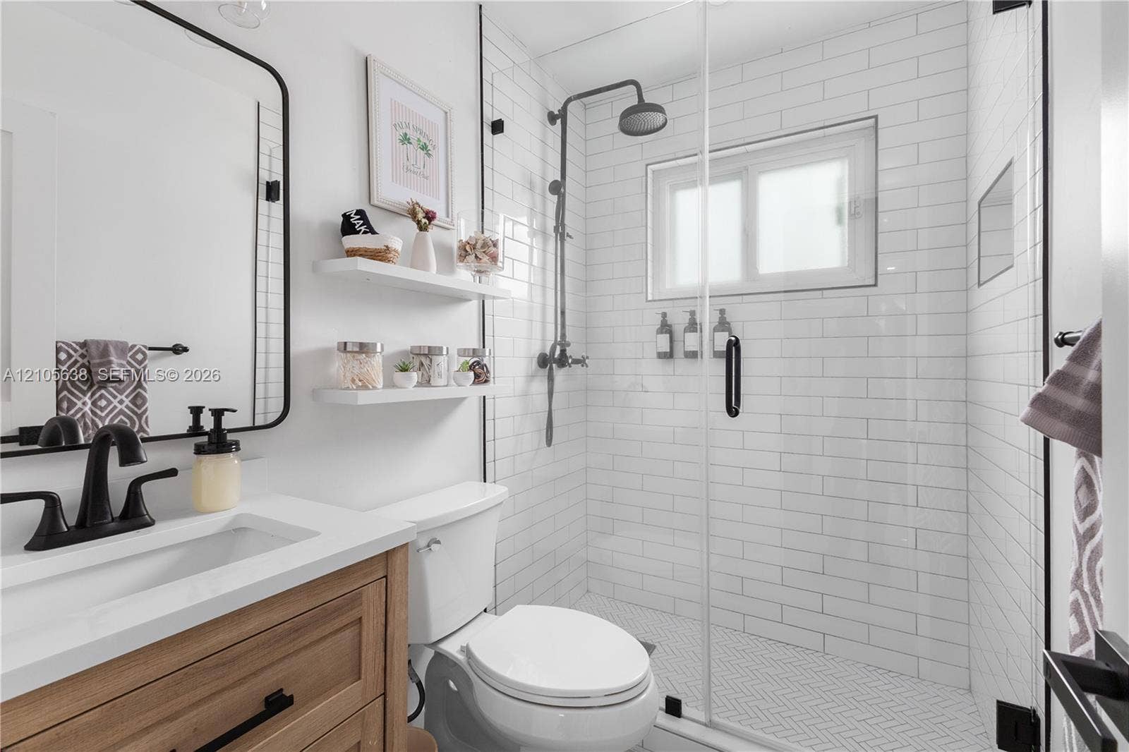 1429 NW 10th Street, #1, Dania, Dania Beach, FL 33004 Bathroom featuring a wood-finish vanity with a white countertop, matte black fixtures, white subway tile shower enclosure with glass door, and wall-mounted shelving