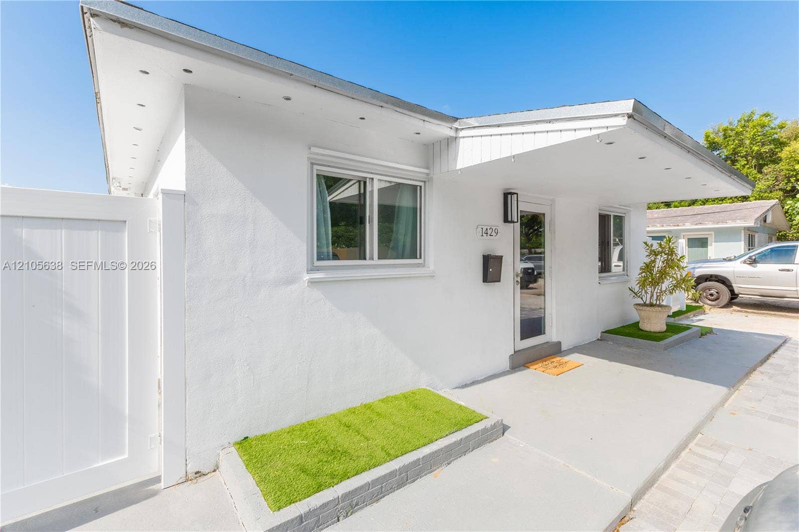 1429 NW 10th Street, #1, Dania, Dania Beach, FL 33004 Exterior featuring smooth white stucco finish, extended roof overhang with integrated lighting, dual-pane windows, and a dedicated concrete porch area with built-in planter beds
