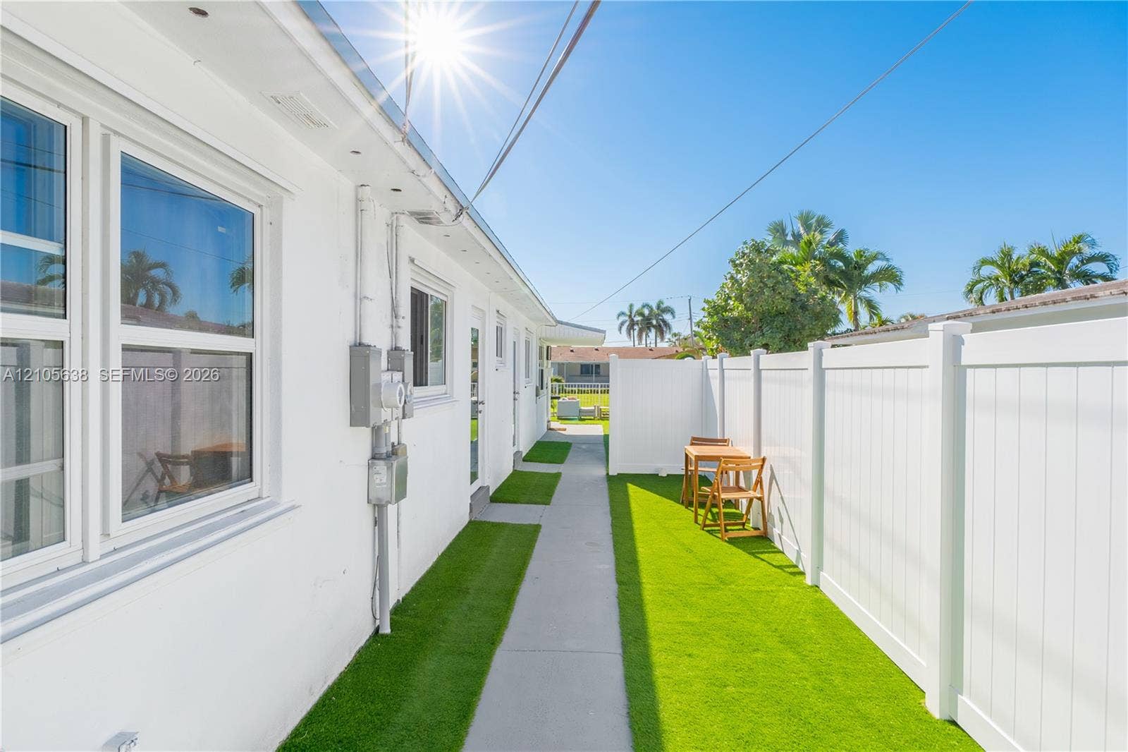 1429 NW 10th Street, #1, Dania, Dania Beach, FL 33004 Exterior side yard featuring white stucco siding, a concrete pathway, artificial turf ground cover, and a full-height white vinyl privacy fence