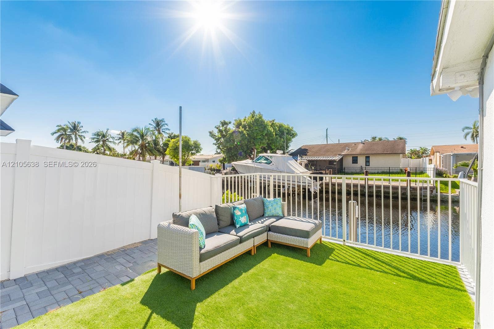 1429 NW 10th Street, #1, Dania, Dania Beach, FL 33004 Waterfront patio featuring synthetic turf, interlocking paver hardscaping, and a white privacy fence with aluminum perimeter railing