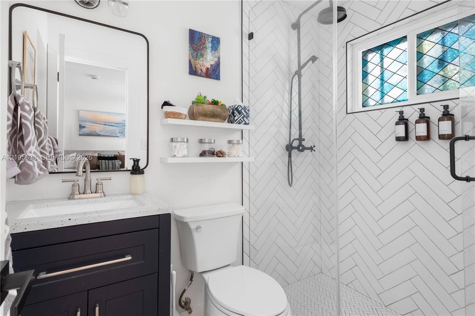 1429 NW 10th Street, #1, Dania, Dania Beach, FL 33004 Bathroom featuring a dark-finish vanity with a speckled countertop, a walk-in shower with white herringbone-patterned wall tile, a glass shower enclosure, and a window with decorative leaded-glass detailing