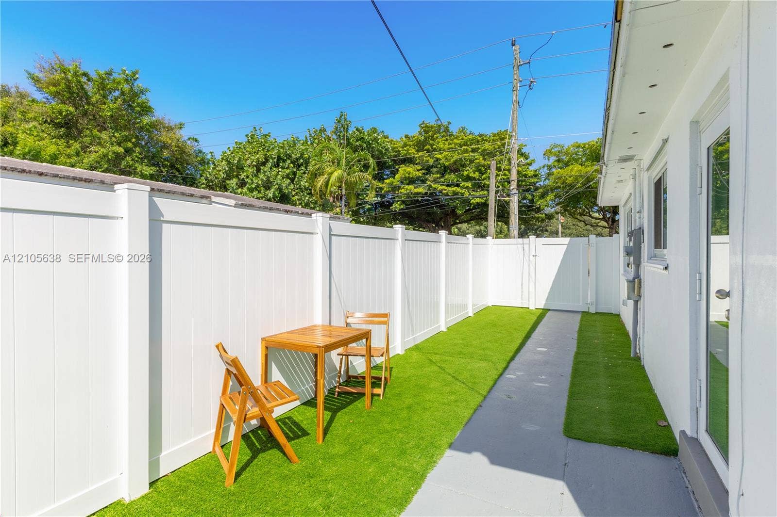 1429 NW 10th Street, #1, Dania, Dania Beach, FL 33004 Exterior side patio featuring synthetic turf, concrete walkway, and white vinyl privacy fencing