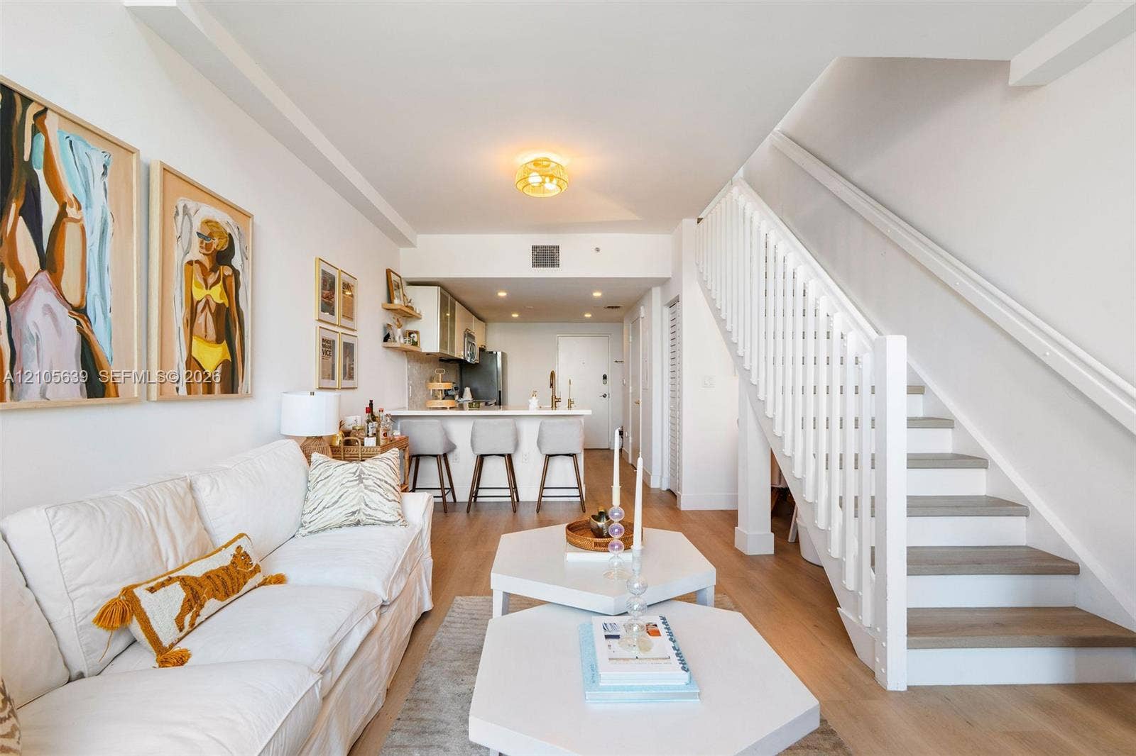 Open-concept interior featuring wood-finish flooring, a white staircase with vertical balusters, a peninsula with stone-finish countertops, and flush-mount lighting