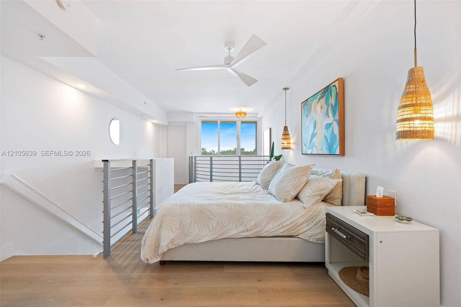 Wood-finish flooring, white three-blade ceiling fan, metal horizontal-bar railings, and woven pendant lighting