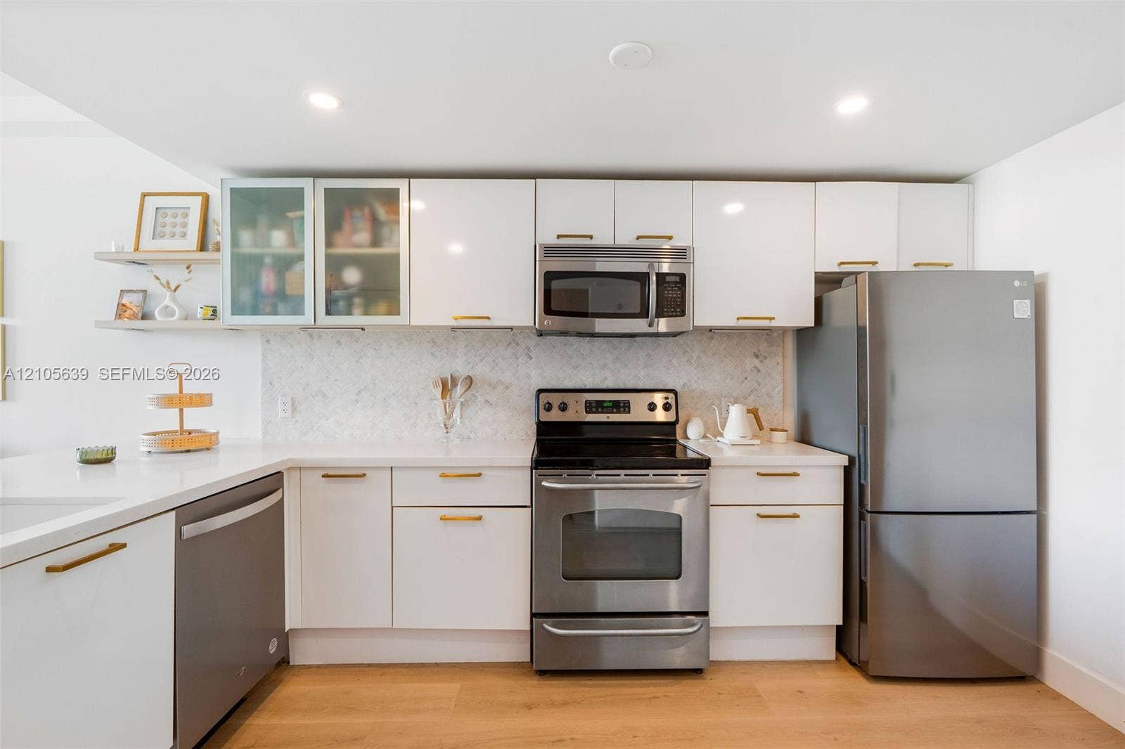 Kitchen featuring flat-panel white cabinetry, herringbone-patterned backsplash, stainless steel appliances, solid-surface countertops, and wood-finish flooring