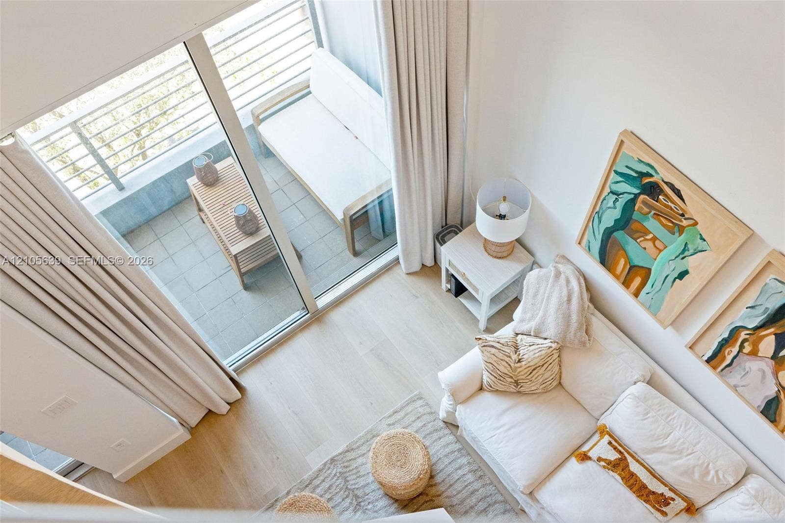 High-ceiling interior with light-toned wood-finish flooring, floor-to-ceiling glass door, and a private balcony with metal railing