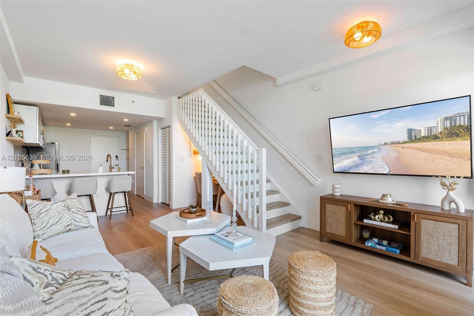 Open-concept living space featuring wood-finish flooring, a white staircase with balusters, built-in kitchen cabinetry, a breakfast bar, and flush-mount lighting fixtures