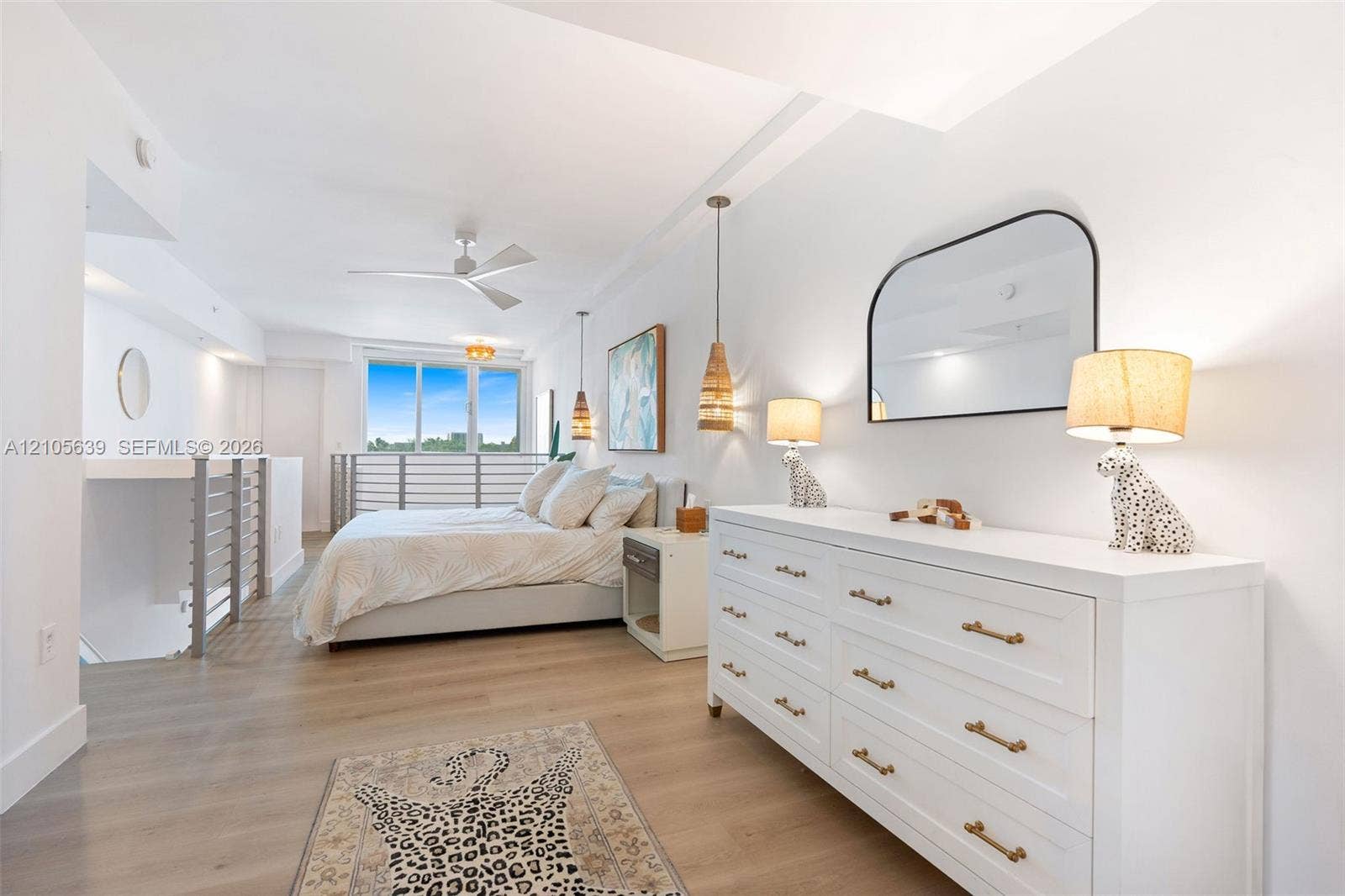 Wood-finish flooring, recessed ceiling lighting, three-blade ceiling fan, arched wall-mounted mirror, and metal railing partition