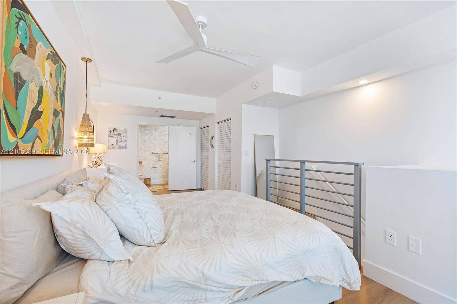 White-painted interior featuring a three-blade ceiling fan, metal horizontal-bar railing, louvered-style closet doors, and wood-finish flooring